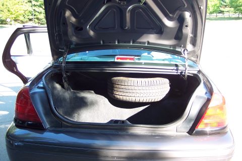2001 Ford Crown Victoria - The trunk of a dark gray sedan is open, revealing a spare tire and the car's interior.