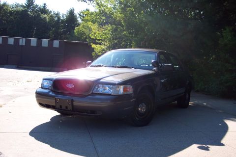 2001 Ford Crown Victoria - A dark sedan, possibly a 2001 Ford Crown Victoria, is parked outdoors with trees and a building in the background.