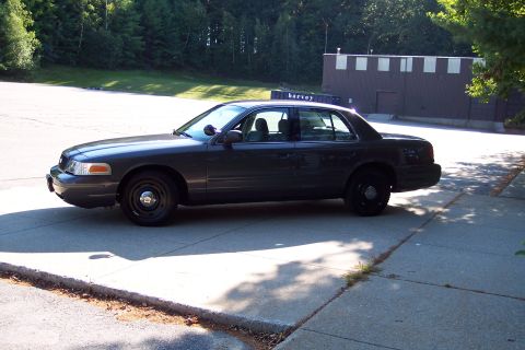 2001 Ford Crown Victoria - A dark gray Ford Crown Victoria police car is parked on a paved surface with a building in the background.