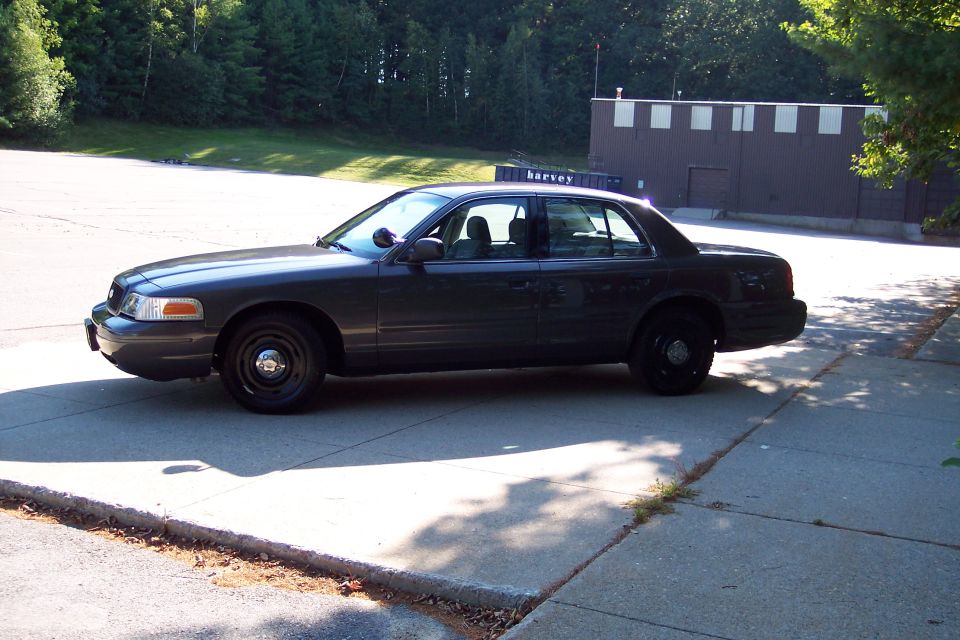 Dark gray Ford Crown Victoria police car parked on pavement. Building in background