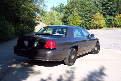 2001 Ford Crown Victoria - A dark gray Ford Crown Victoria is seen from a three-quarter rear view, parked outdoors on a sunny day.