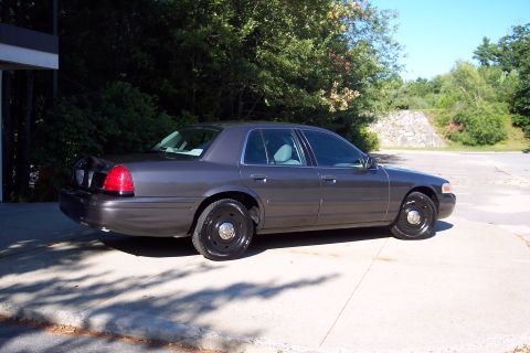 2001 Ford Crown Victoria - A 2001 Ford Crown Victoria sedan is parked on a concrete surface with trees in the background.