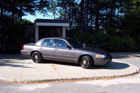 2001 Ford Crown Victoria - A gray 2001 Ford Crown Victoria is parked on a concrete surface with trees in the background.