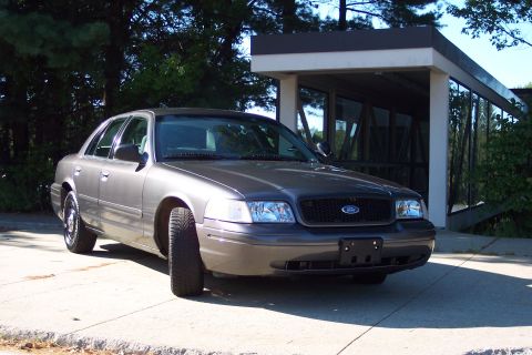 2001 Ford Crown Victoria - Ford Crown Victoria parked on a concrete driveway near a building with large windows.