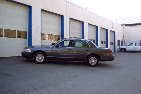 2001 Ford Crown Victoria - A 2001 Ford Crown Victoria is parked outside a commercial building next to a white pickup truck.