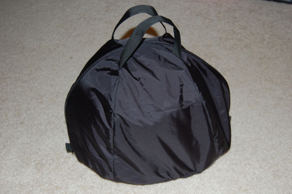 Black nylon helmet bag with two fabric handles on a carpeted floor