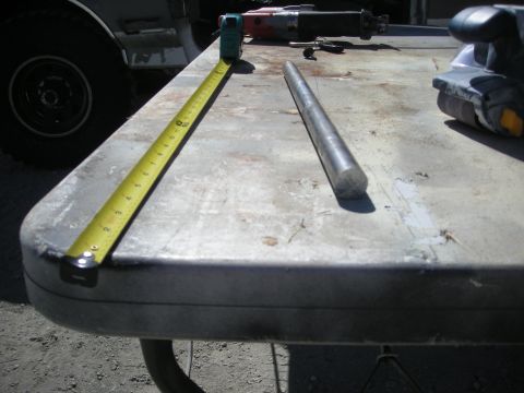 1991 Ford Bronco - A metal rod and tape measure are laid out on a table, with tools and a vehicle visible in the background.