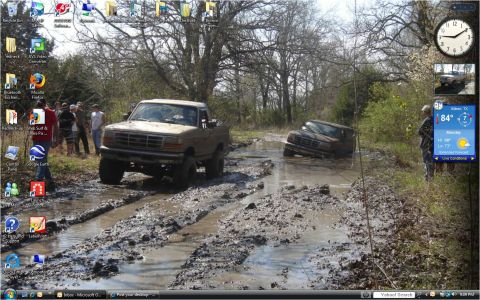 1996 Ford Bronco - Two pickup trucks are stuck in deep mud on a wooded trail, with several people observing.