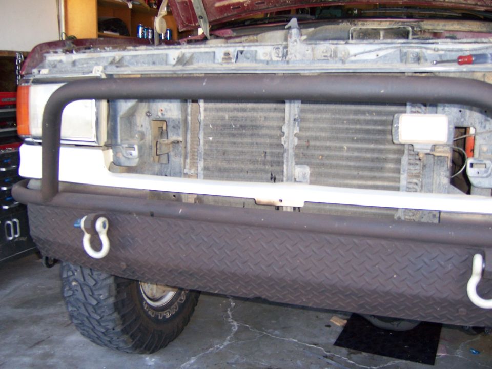 Truck front end with a diamond plate bumper and tow hooks. Hood is open showing the radiator