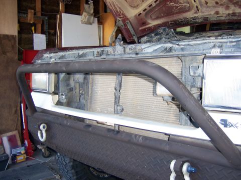 1991 Ford Bronco - The front end of a vehicle is visible with the hood open, revealing the radiator and grille area.