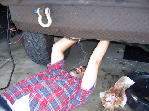 1991 Ford Bronco - A person is working on the underside of a vehicle, with tools and fluids nearby.