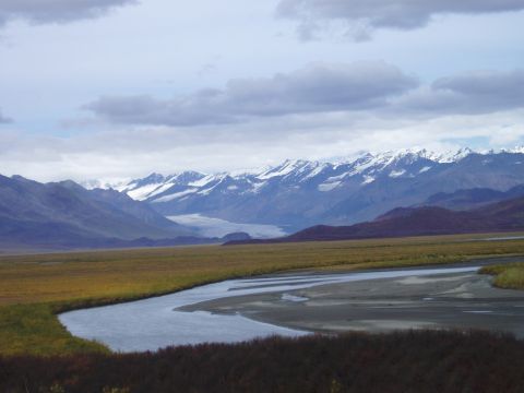 2000 Ford E350 - A wide river flows through a grassy plain towards a mountain range under a cloudy sky.