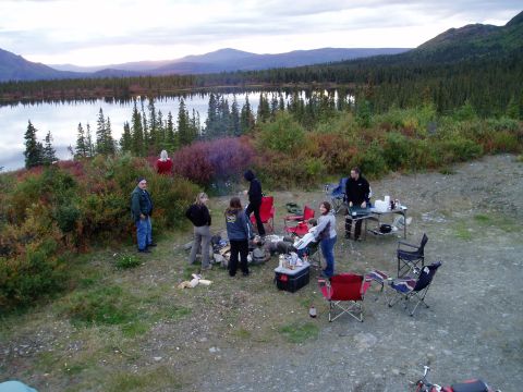 2000 Ford E350 - A group enjoys a campfire at a scenic lakeside location with mountains and trees.