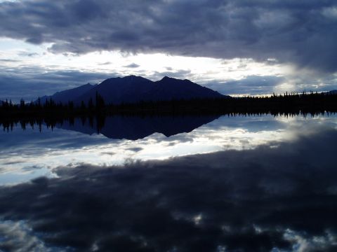 2000 Ford E350 - A vast mountain range is mirrored in the still waters of a lake, with dramatic clouds overhead.