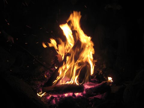 2000 Ford E350 - A campfire burns brightly at night, with embers glowing and sparks rising into the darkness.