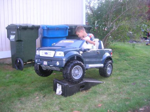 1996 Ford Bronco - A child sits in a toy truck that is positioned on a ramp in a grassy yard.