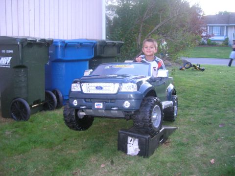 1996 Ford Bronco - A child sits in a toy Ford F-150 truck parked on blocks next to trash bins.