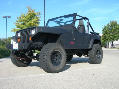 1991 Jeep Wrangler - This black 1991 Jeep Wrangler features off-road tires and a custom front bumper, parked outdoors under a clear blue sky.