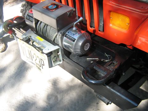 1990 Ford Bronco - A winch is mounted to the front bumper of an orange Jeep, with a license plate attached.