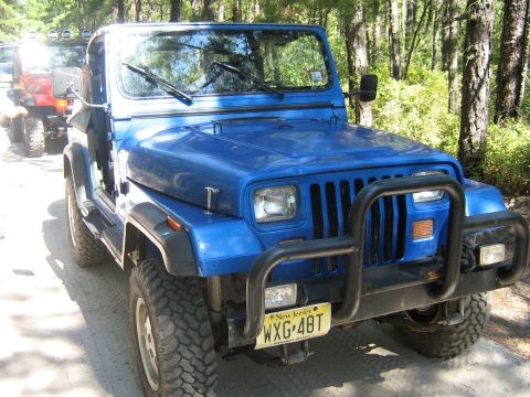 1990 Ford Bronco - A blue Jeep Wrangler is parked on a dirt road, with another vehicle visible behind it.