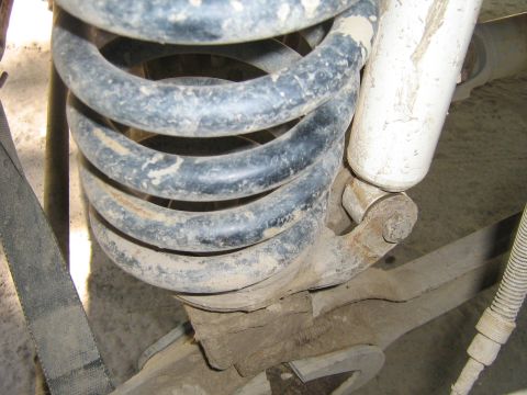 1990 Ford Bronco - This image shows a close-up view of a vehicle's suspension system, specifically a coil spring and shock absorber, covered in dirt.