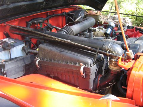 1990 Ford Bronco - The engine compartment of an orange Jeep is shown, the air filter housing and battery.