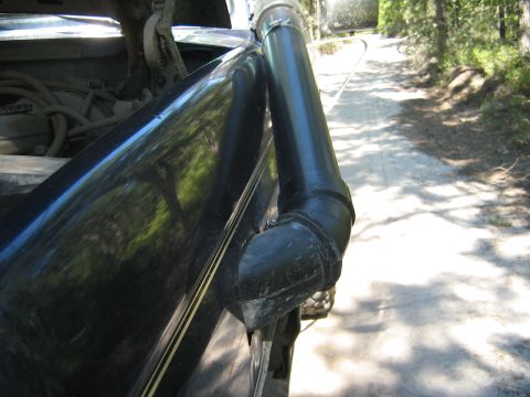1990 Ford Bronco - A black vehicle with a snorkel attachment is driving on a dirt road through a wooded area.