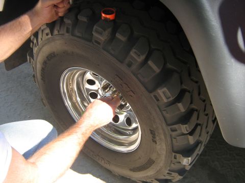 1990 Ford Bronco - Hands work on a large off-road tire mounted on a chrome wheel.