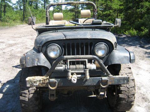 1990 Ford Bronco - This Jeep CJ-7 features a winch and a custom front bumper, seen on a dirt road.