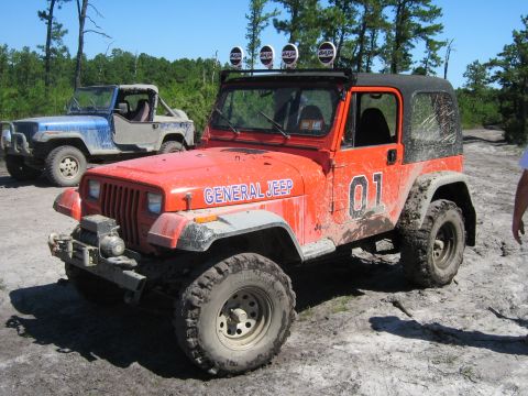 1990 Ford Bronco - This orange Jeep, labeled "GENERAL JEEP" and "01", is equipped for off-road use with prominent tires and a light bar.