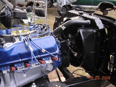 1978 Ford Bronco - Close-up of a blue Ford V8 engine assembly, with a radiator and fan in the foreground and other vehicles in the background.