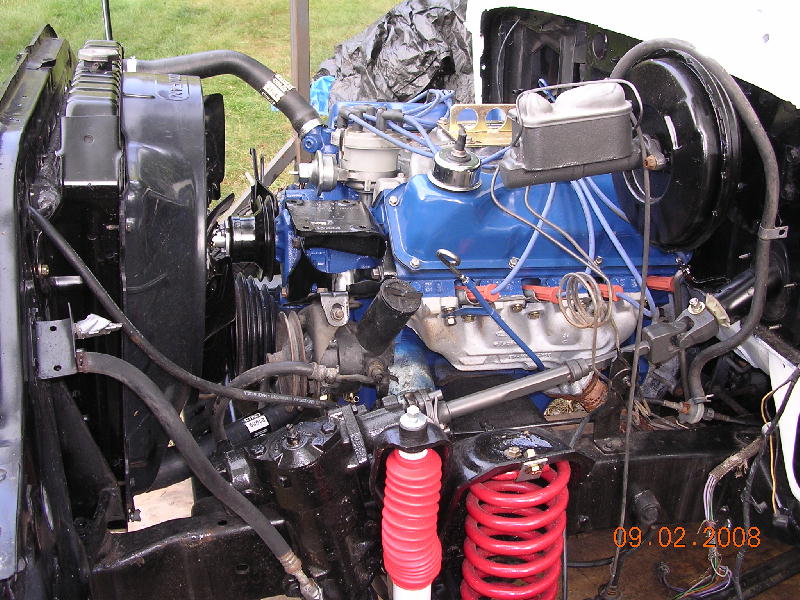 Engine bay with blue Ford V8 engine, red coil springs, and black radiator