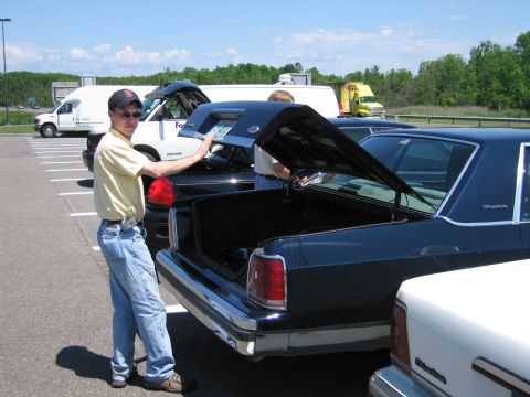 2001 Ford Crown Victoria - A man stands by the open trunk of a dark blue sedan in a parking lot with other vehicles and trucks visible.