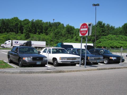 2001 Ford Crown Victoria - A row of sedans, including a dark gray 2001 Ford Crown Victoria, are parked in a lot under a clear blue sky.