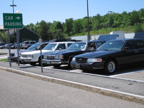 2001 Ford Crown Victoria - A row of Crown Victoria police cars are parked in a lot, with a sign indicating car parking.