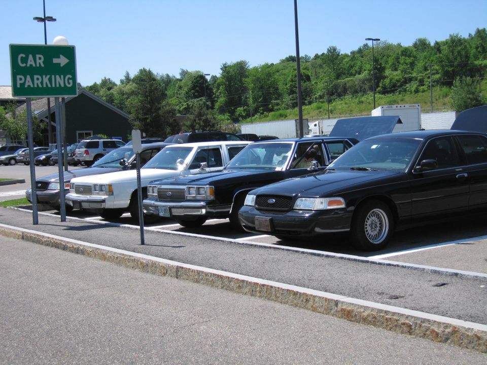 Several police cars parked in a lot, one black Crown Victoria in foreground