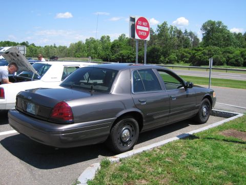 2001 Ford Crown Victoria - Two cars parked, one with hood up, near a highway and a do not enter sign.