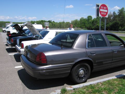 2001 Ford Crown Victoria - Several cars are parked in a lot with their trunks open, including a dark gray police car in the foreground.