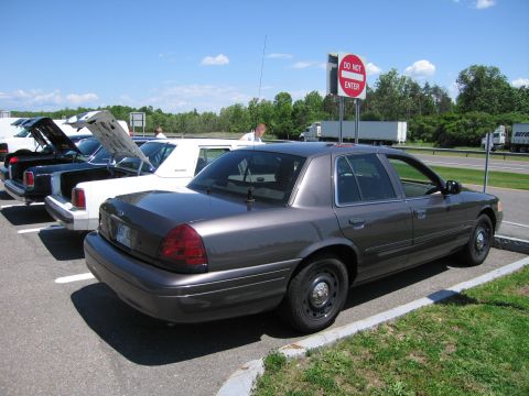 2001 Ford Crown Victoria - A row of sedans are parked, with their trunks and hoods open, under a bright blue sky.
