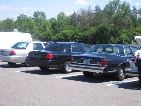 2001 Ford Crown Victoria - A line of Ford Crown Victorias, including black, silver, and dark blue models, are parked in an outdoor lot.