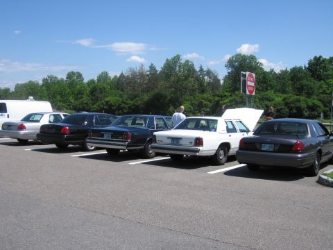 2001 Ford Crown Victoria - Several police interceptor sedans are parked in a lot on a sunny day.