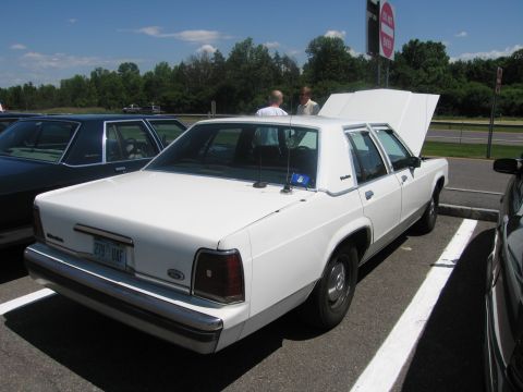 2001 Ford Crown Victoria - A white sedan is parked with its hood open, viewed from the rear quarter panel.