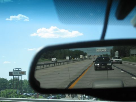 2001 Ford Crown Victoria - A black 2001 Ford Crown Victoria is seen driving on a highway, reflected in the rear-view mirror.