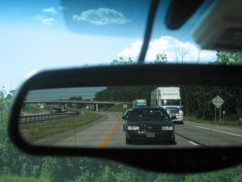 2001 Ford Crown Victoria - View of highway traffic from a car's rearview mirror, showing a black sedan and a semi-truck.