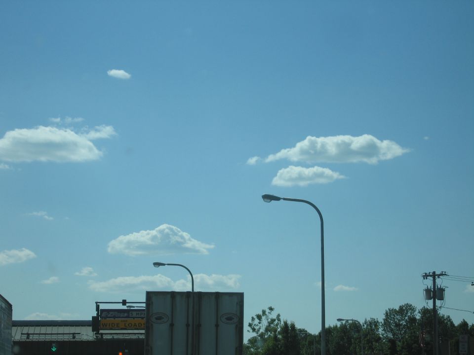 Blue sky with scattered clouds, two streetlights, and distant trees