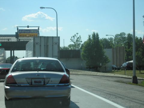2001 Ford Crown Victoria - A silver sedan approaches a toll booth with a 'WIDE LOADS' sign visible overhead.