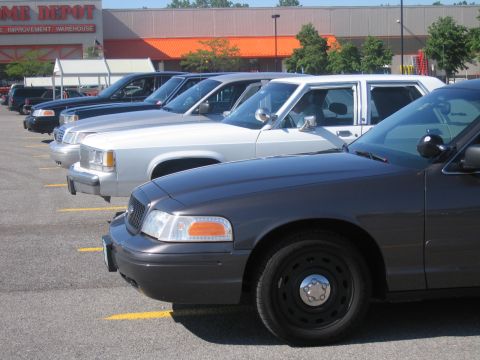 2001 Ford Crown Victoria - A line of police cars, including a dark gray Ford Crown Victoria, parked in a lot in front of a Home Depot.