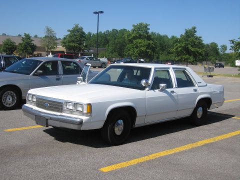2001 Ford Crown Victoria - A white sedan is parked in a lot with its driver's door ajar.