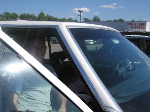 2001 Ford Crown Victoria - Man smiles from the driver's seat of a white sedan parked in a lot with a Tire & Lube Express in the background.