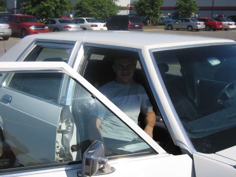 2001 Ford Crown Victoria - Man sits in the driver's seat of a white sedan with the passenger door open.
